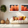A cosy living room with a white curved sofa, colourful pillows, a leafy potted plant, woven side table, sunlight streaming in, and the 'Faunus' Diptych Print with orange flower close-ups—a tranquil retreat.