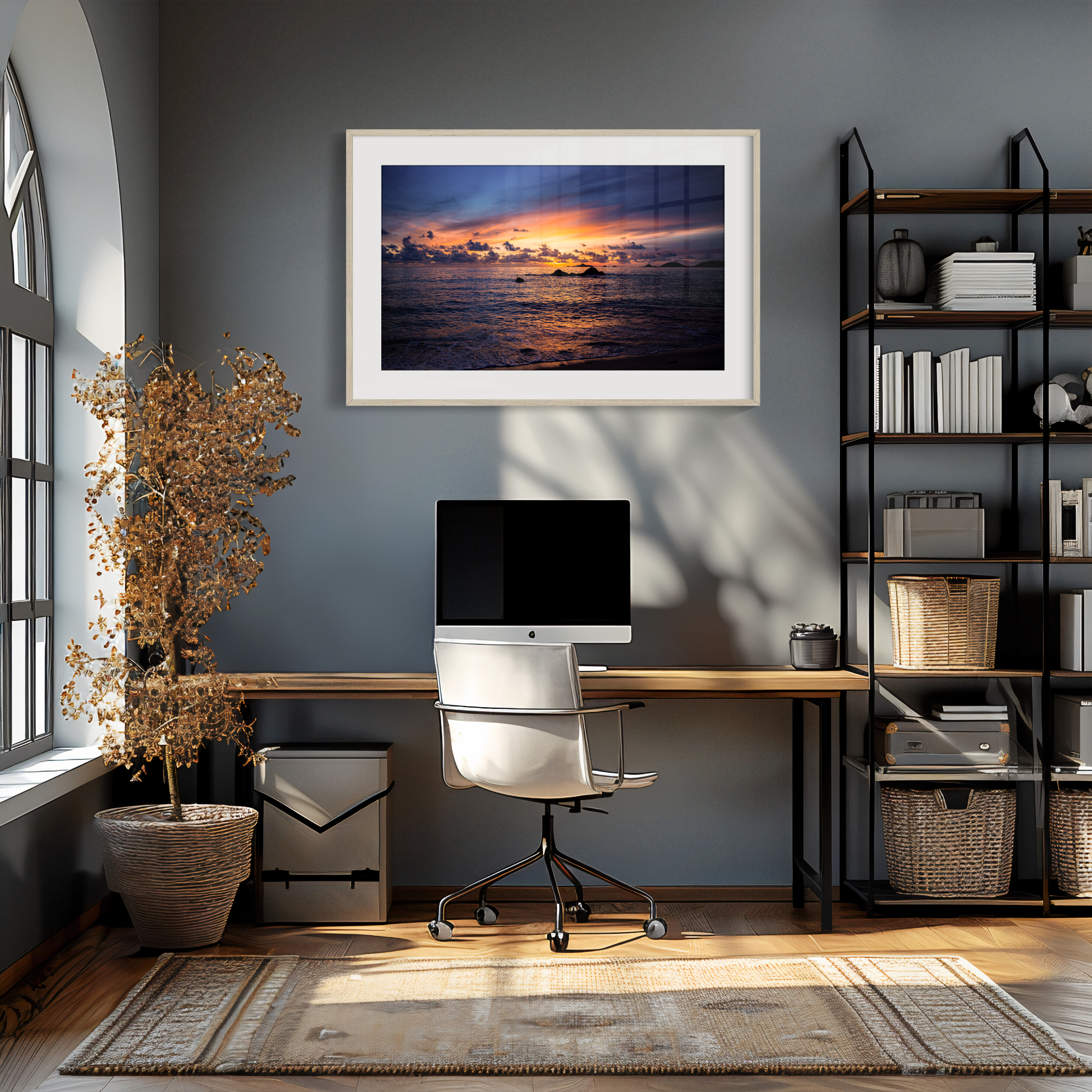 A modern home office with a desk, white chair, computer, and shelves sits by a large arched window. Above the desk, the ‘Fire in the Sky’ Print warms the grey wall. A dried plant adds a natural touch in the corner.