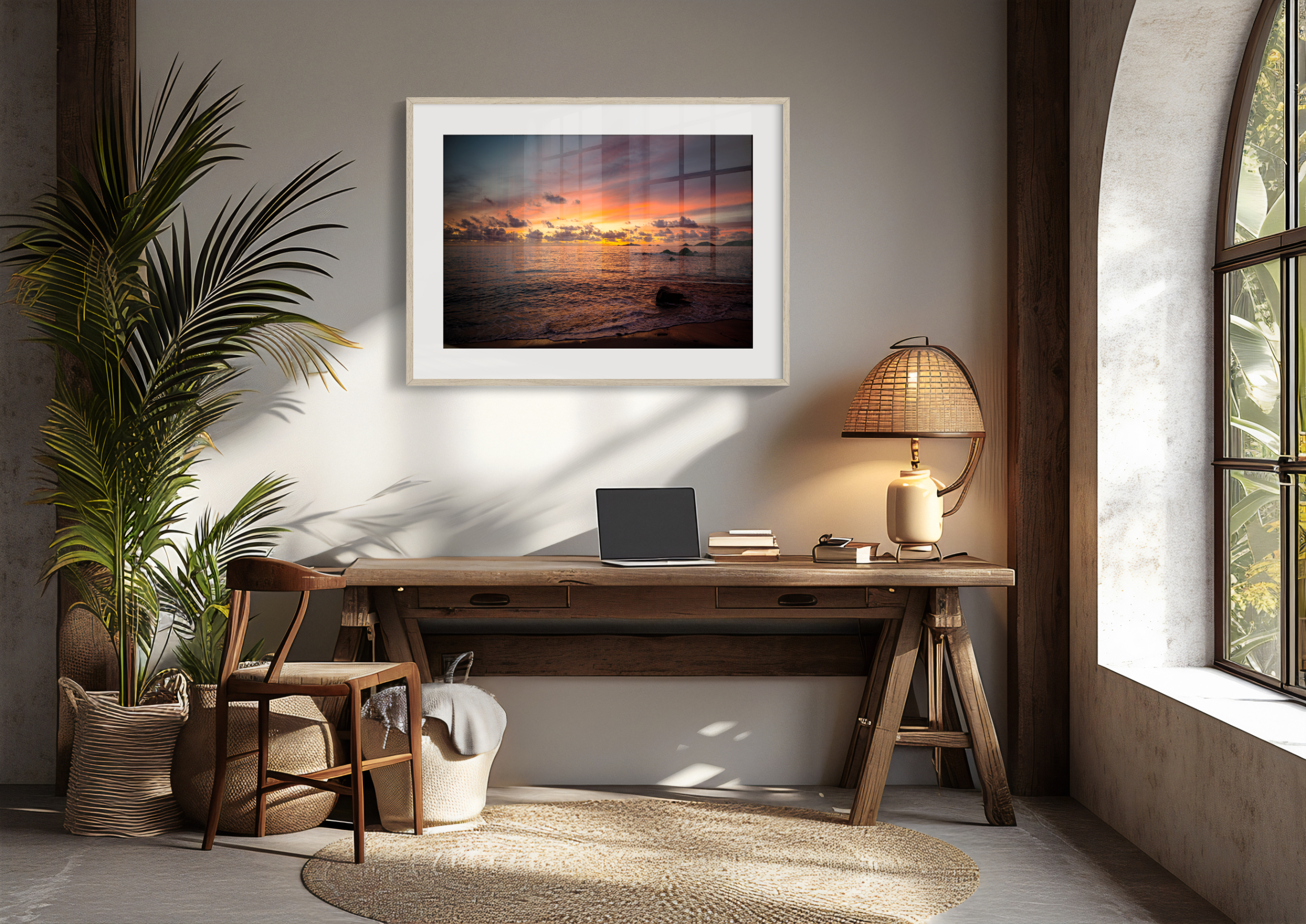 A cosy home office features a wooden desk, chair, laptop, basket, a large framed 'Island Horizon' Print of a sunset beach, tall leafy plant, woven lamp, and natural sunlight shining through an arched window.