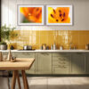A modern kitchen with light green cupboards, a white worktop, yellow tiled splashback, and the 'Lilium' Diptych Prints featuring abstract orange floral art above the counter. A potted plant and kitchenware decorate the counter and table.