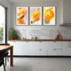 A modern kitchen with white cupboards, wooden worktops, and potted plants features the 'Lilium' Triptych Print—three framed close-up photos of orange Lilium flowers—above the sink on a white tiled splashback.