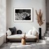 A modern, minimalist living space with a white cushioned bench, round cushions, a wooden table, a tall black vase with pampas grass, and the 'Lunar' (H) Print—a large black-and-white lunar-inspired photograph—on the wall.