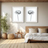A cosy bedroom features a wooden bed with white bedding and neutral decor. Above the bed hangs the 'Dimorphotheca' Diptych Print, while a large potted plant sits beside a woven ottoman and small wooden table.