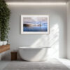 A modern bathroom with a freestanding white bath, wooden double-sink vanity, large window, leafy green plant, and the 'Pier of Bastia' print framed above the bath.