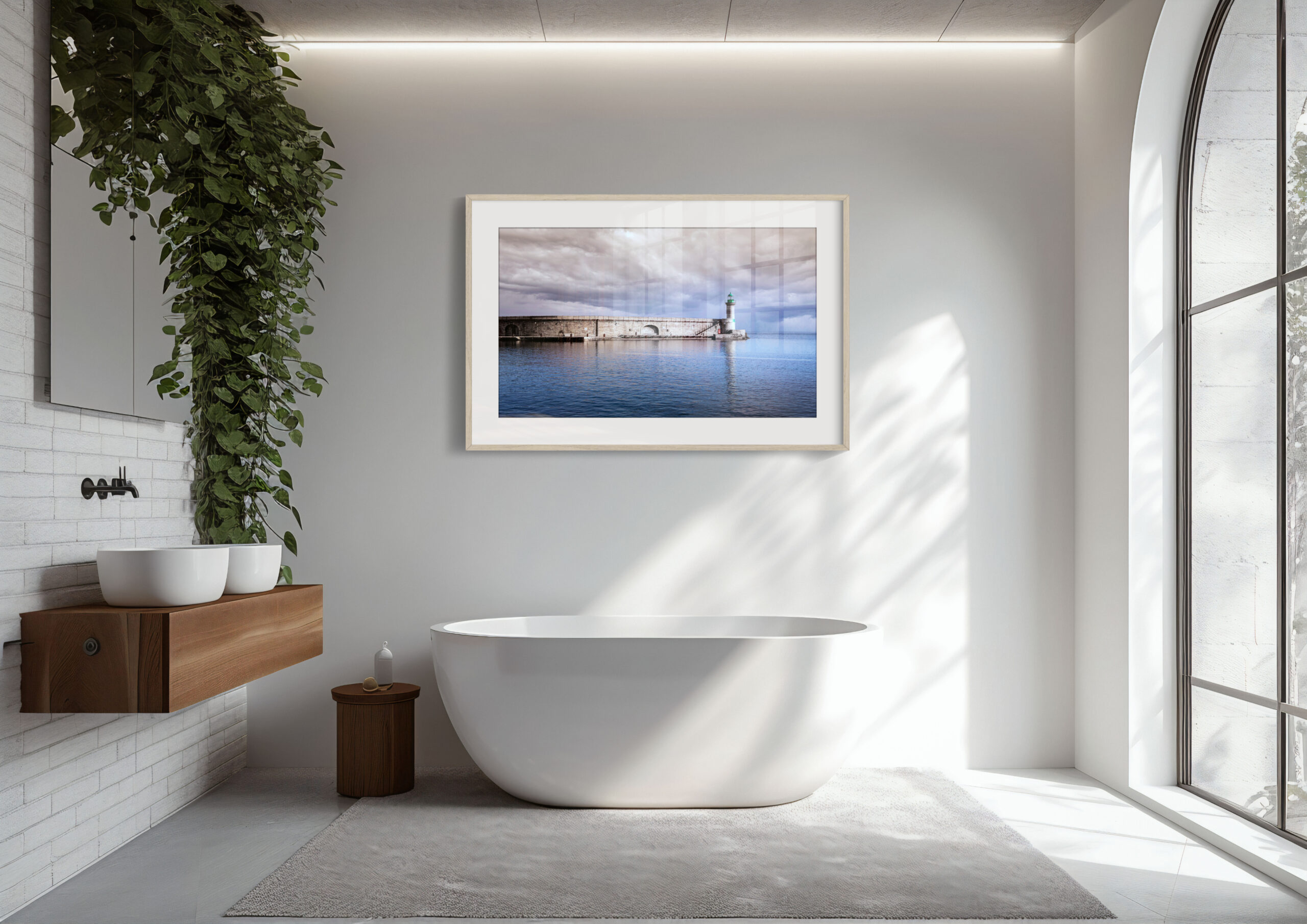 A modern bathroom with a freestanding white bath, wooden double-sink vanity, large window, leafy green plant, and the 'Pier of Bastia' print framed above the bath.