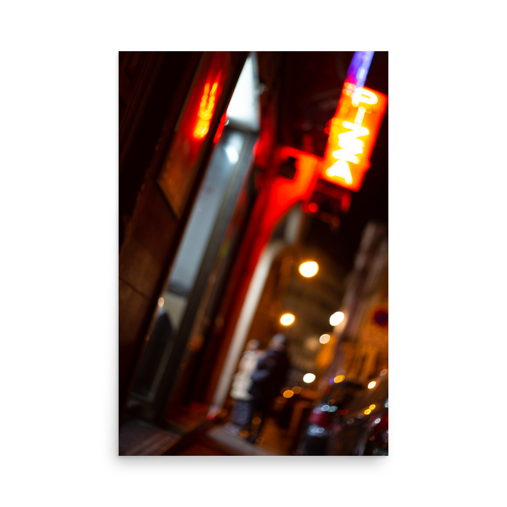The 'Nights in Marseille' Print captures an out-of-focus nighttime street scene with blurred shopfronts, a glowing red neon sign, streetlights, and indistinct figures walking along the pavement near parked cars.