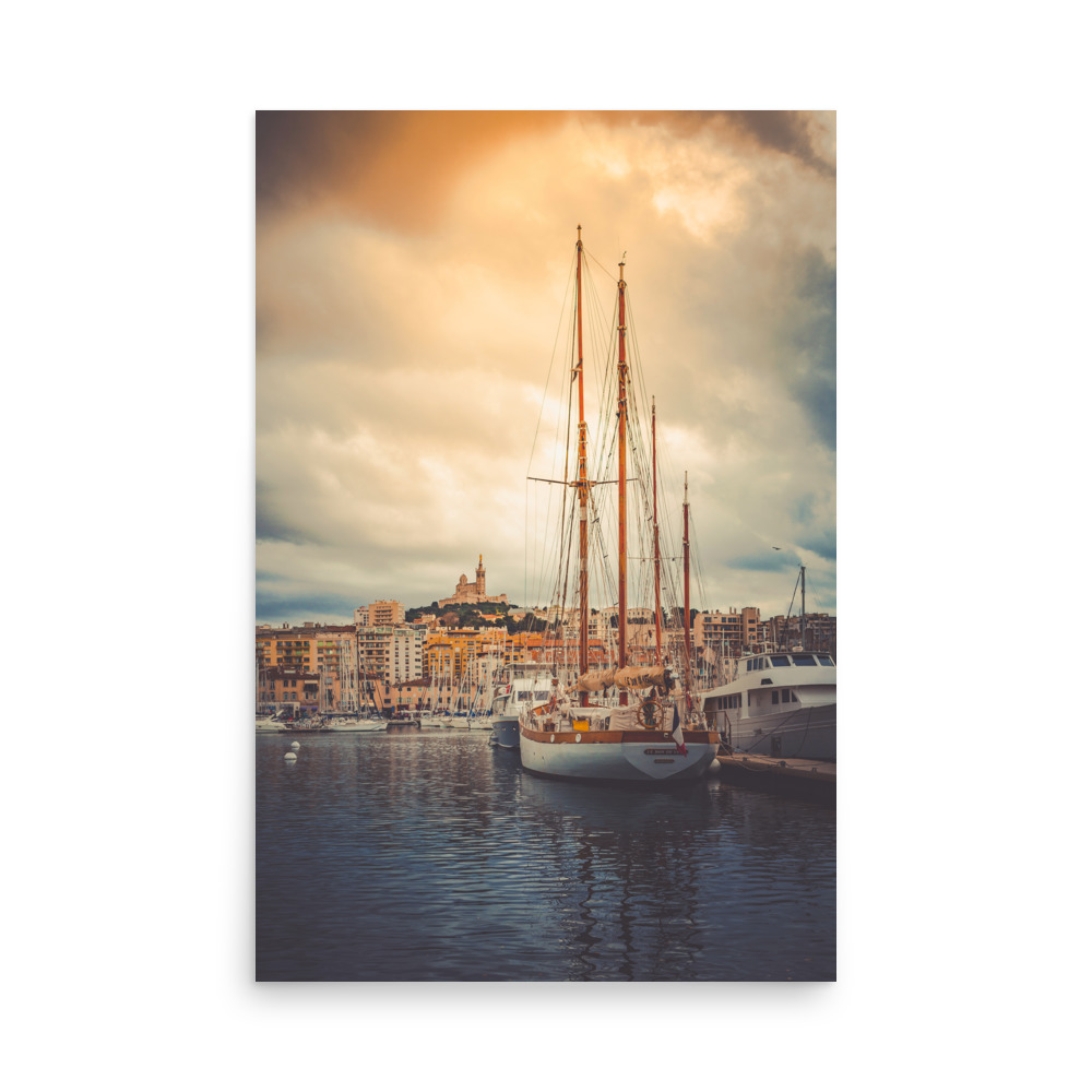 The 'Winter Sails' Print features a sailboat moored in a peaceful marina at sunset, set against city buildings and a hilltop church beneath a dramatic, cloudy sky.