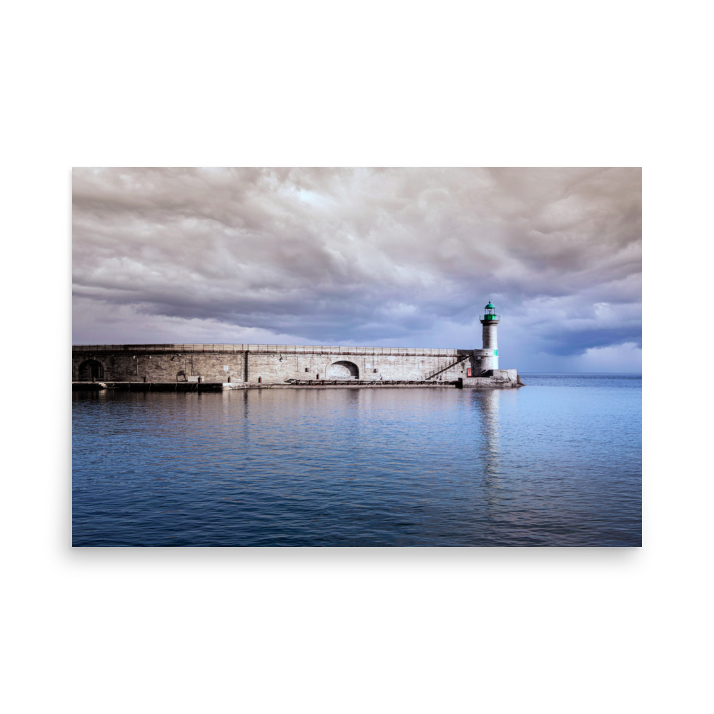 The 'Pier of Bastia' Print features the landmark’s green-topped lighthouse stretching into tranquil blue water beneath a striking, cloud-filled sky.