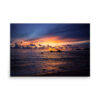 The 'Fire in the Sky' Print captures a vibrant sunset over the ocean, dramatic clouds, small distant islands, and gentle waves reflecting orange and purple near a sandy shore.