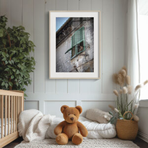 A cosy nursery features a cot, plush bear, soft blankets, plants, and a framed 'Neighbourhood Watch' print showing a cat peering from a green-shuttered window in an old building.