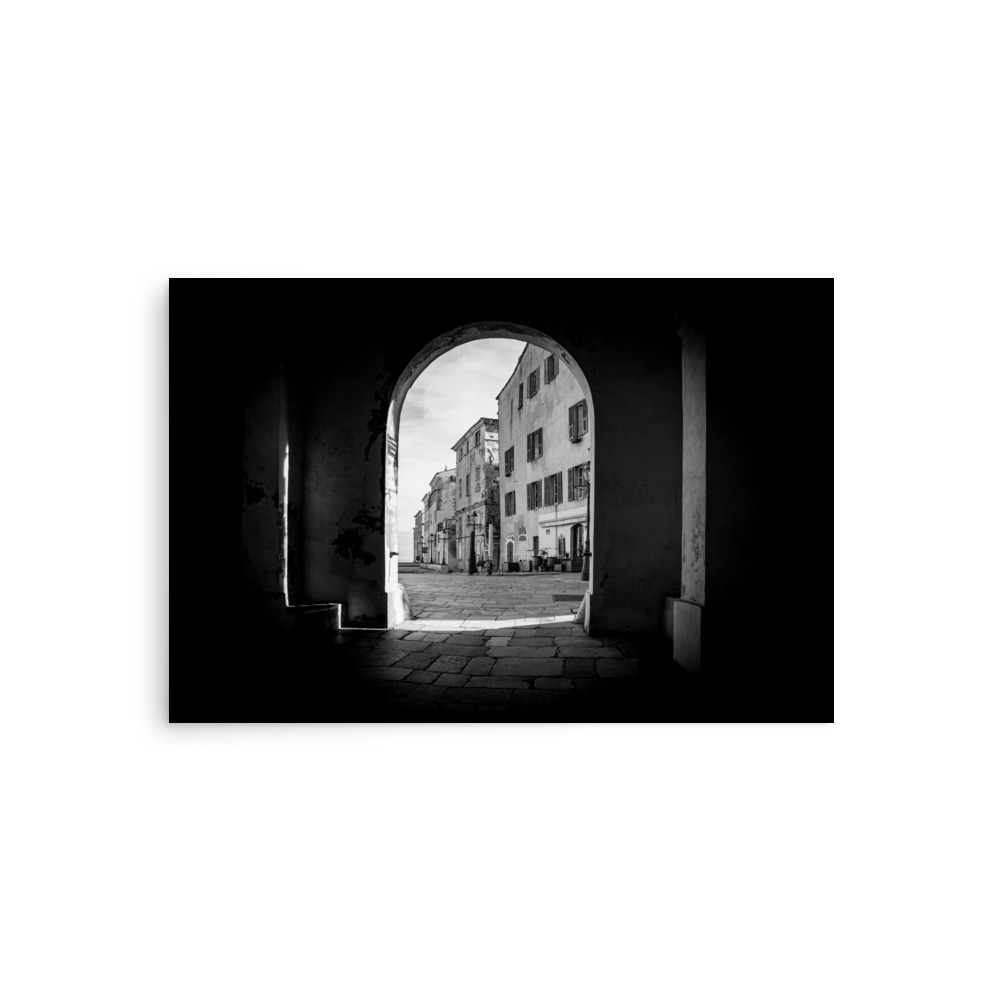 The "Arch of the Citadel" Print features a black-and-white photo of a European street framed by a stone archway, with historic buildings and an illuminated cobbled path beyond the shadowy arch.