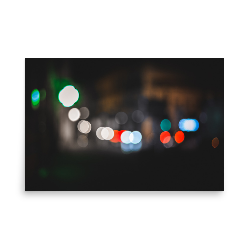 A blurred, out-of-focus night scene with various circular lights in white, green, red, and blue against a dark background, creating a bokeh effect.